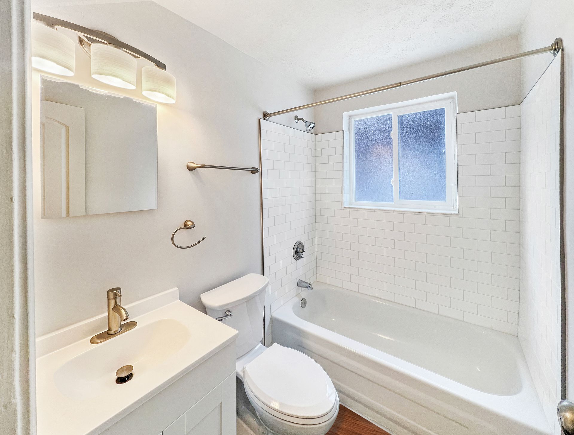 Bathroom with white tile, a bathtub, toilet, and sink, and a frosted window.