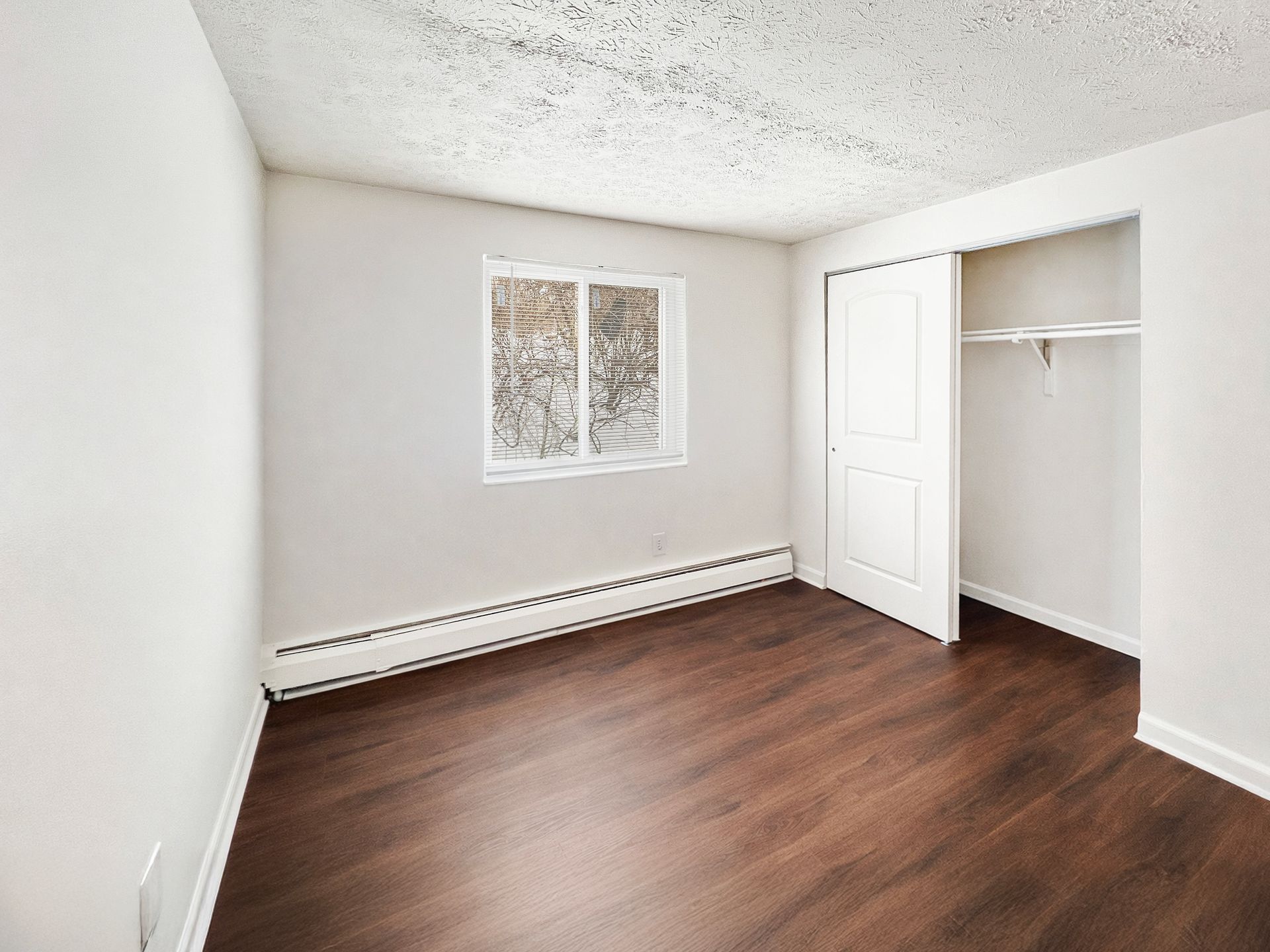 Empty bedroom with white walls, dark wood floor, and a closet.