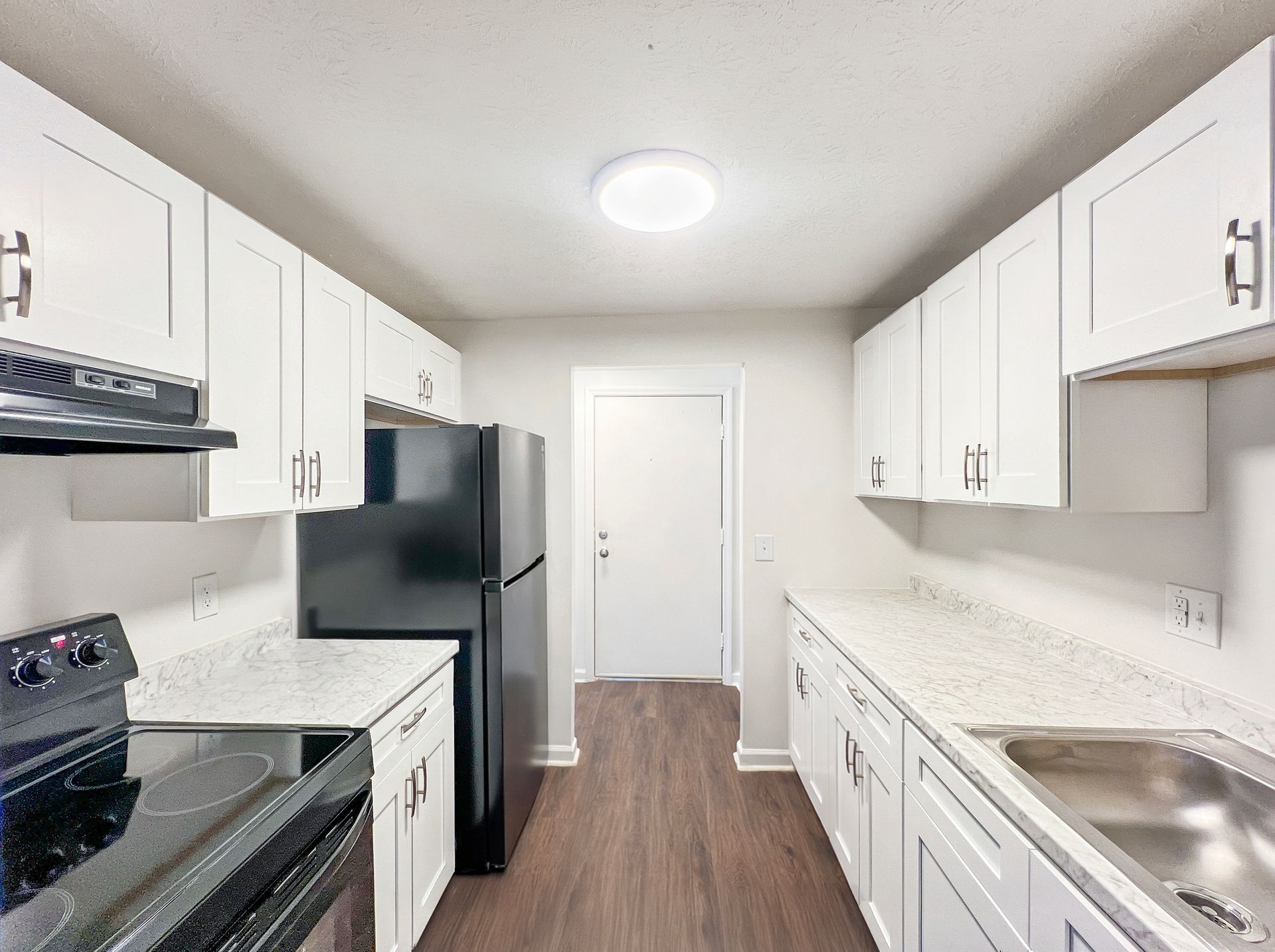 White kitchen with black appliances, white countertops, and wood-look flooring.