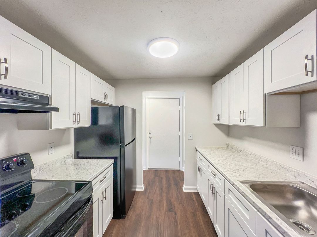 White kitchen with brick wall, wooden counters, white cabinets, and plants.