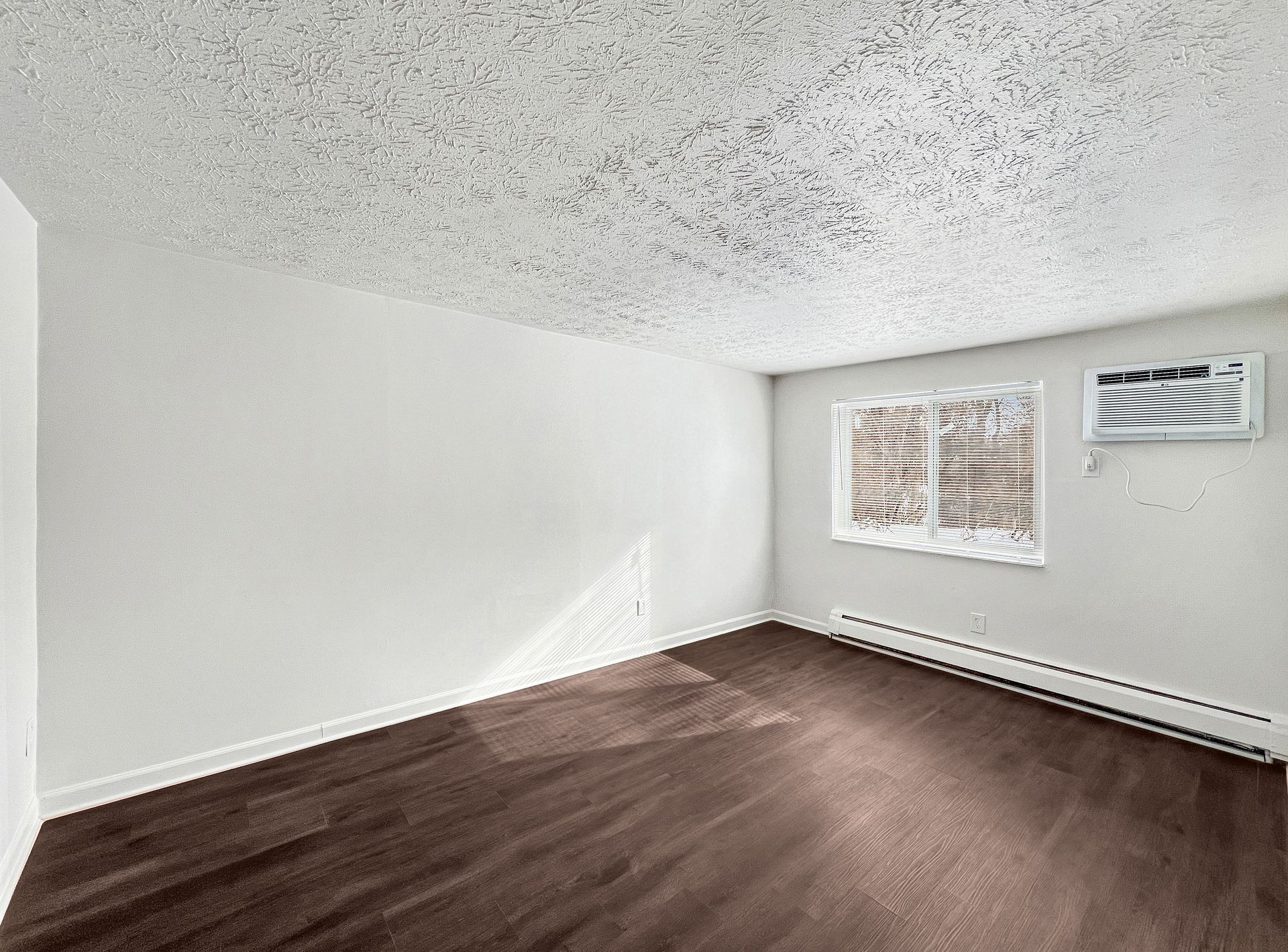 Empty room with dark wood floor, white walls and textured ceiling. Window with radiator.