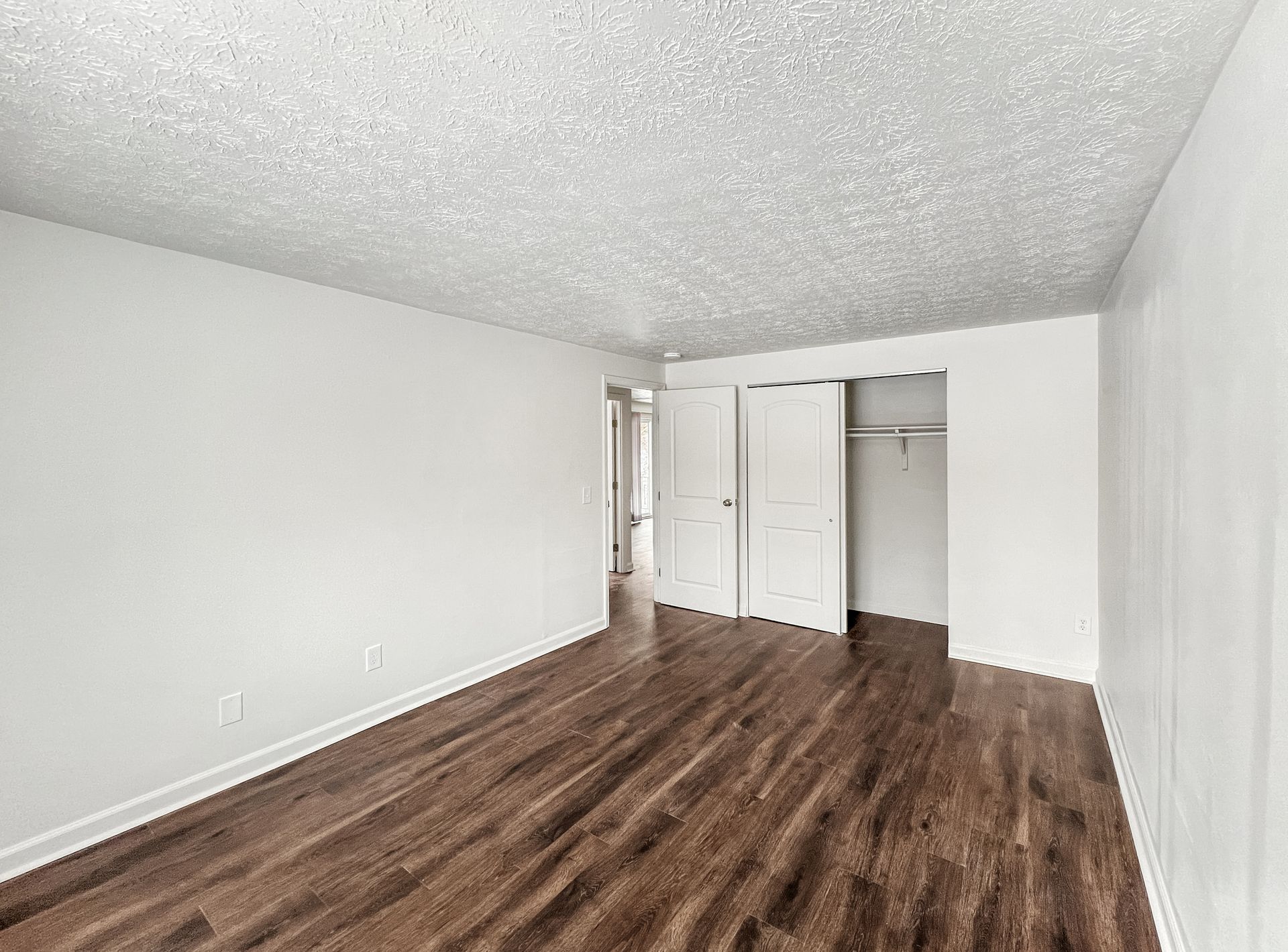Empty room with wood-look floor, white walls, and a closet with open doors.