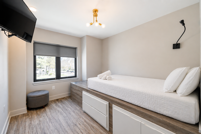 Bright small bedroom with a single bed, window, gray walls, and wall-mounted TV
