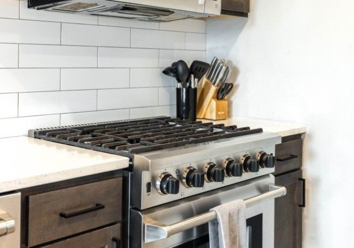 Stainless steel gas range in modern kitchen with white tile backsplash.