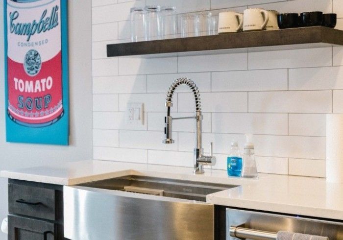 Kitchen with stainless steel sink, pull-down faucet, white subway tile backsplash, and floating shelf with glasses and mugs.