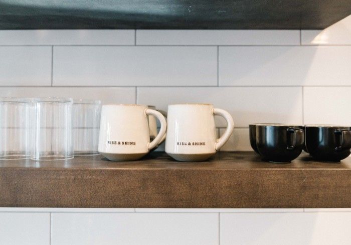 Shelf with two cream mugs, two black bowls, and clear glasses.