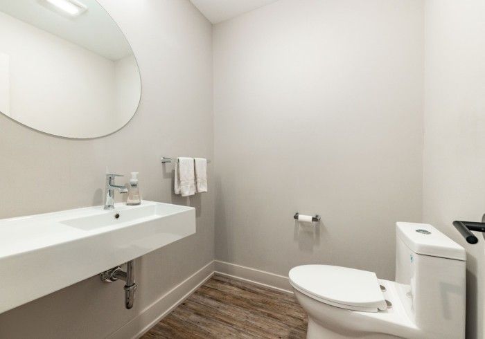 Modern powder room: white sink, toilet, round mirror, neutral walls, wood-look floor.