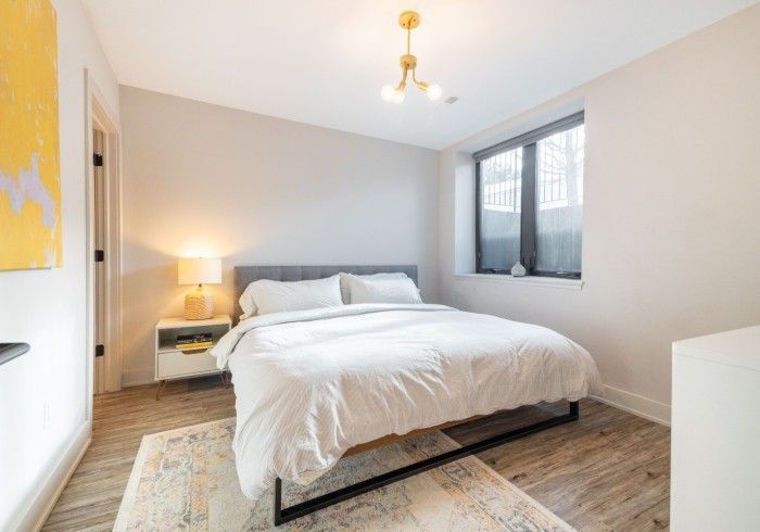 Bedroom with bed, nightstand, rug, window, and modern light fixture. Soft neutral colors.