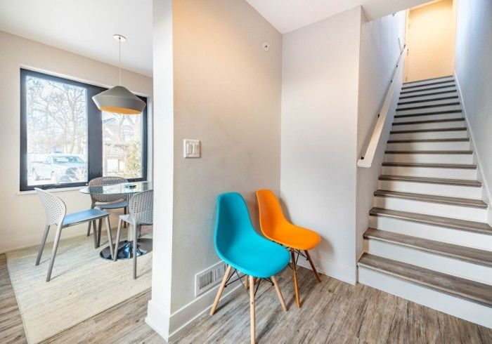 Entryway with stairs and modern chairs; dining area visible. Turquoise and orange chairs.