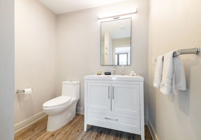 White bathroom with toilet, vanity, mirror, and towel rack.