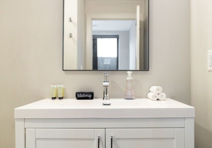 White bathroom vanity with mirror, faucet, and toiletries.