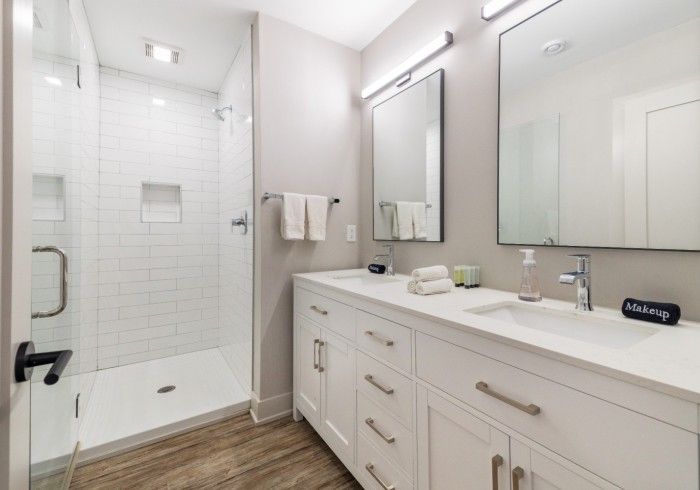 Modern bathroom with white cabinets, double sinks, and a glass-enclosed shower.