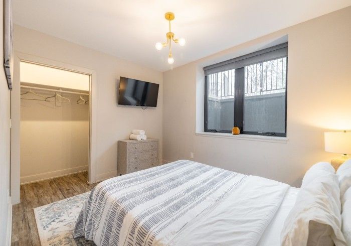 Bedroom with bed, closet, TV, window, and dresser. Neutral tones, modern design.