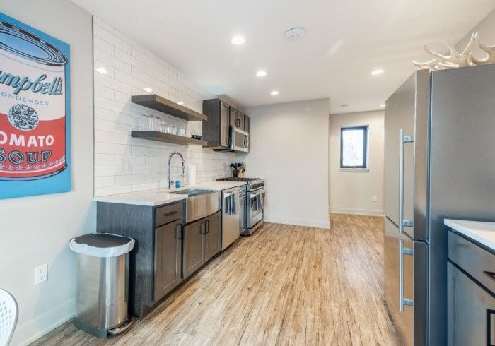 Modern kitchen with stainless steel appliances, dark cabinets, and wood-look flooring. A large pop art painting hangs on the wall.