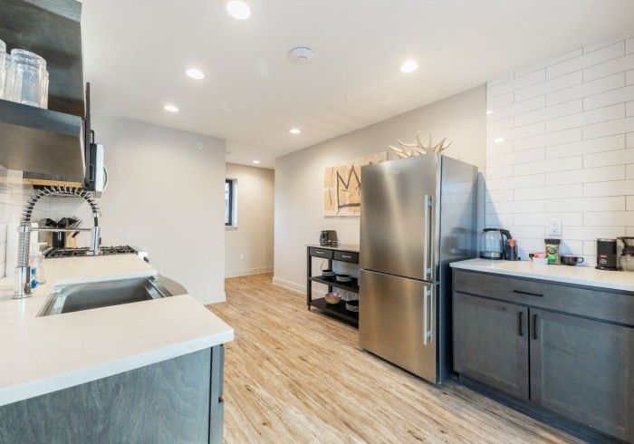 Modern kitchen with gray cabinets, stainless steel refrigerator, and light wood flooring.