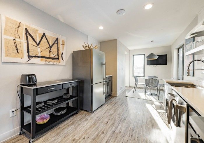 Modern kitchen with black cart, stainless steel fridge, and art, light wood floors.
