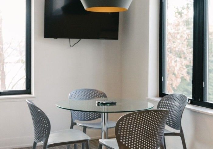 Dining area with round glass table, gray chairs, TV, and large windows.