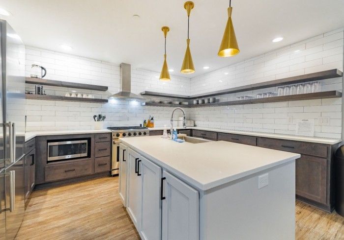 Modern kitchen with white countertops, wooden floors, and gold pendant lights.