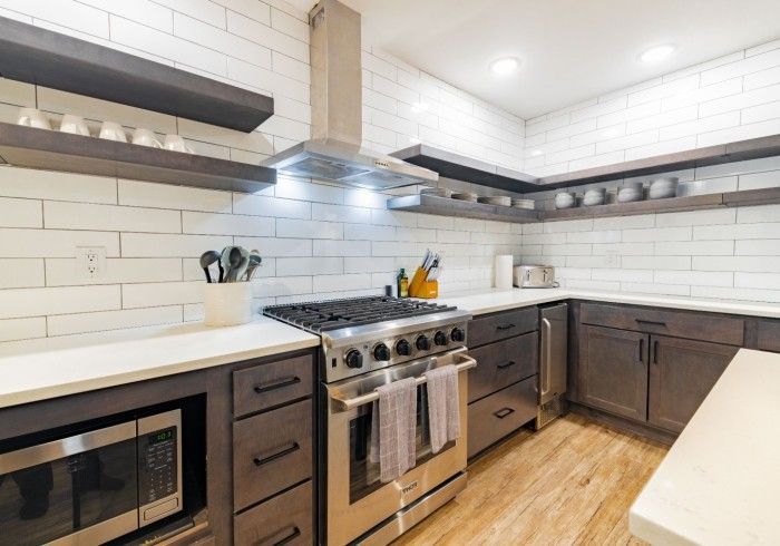 Modern kitchen with dark cabinetry, white countertops, stainless steel appliances, and white subway tile backsplash.
