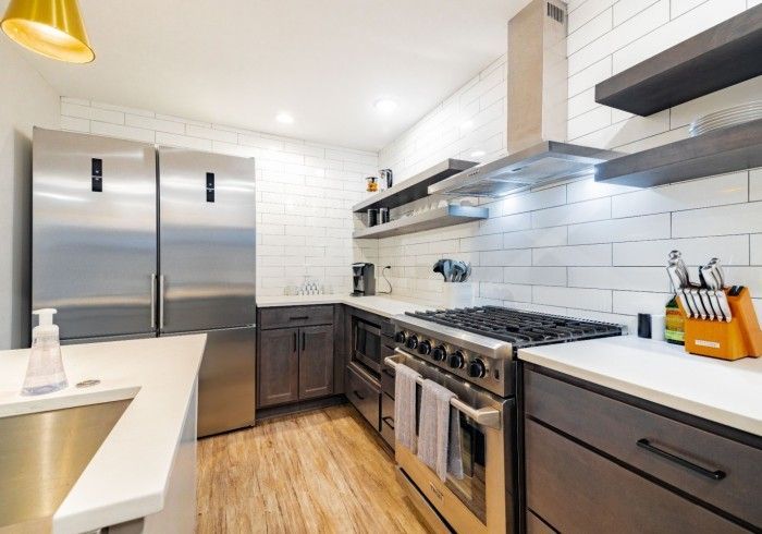Modern kitchen with stainless steel appliances, grey cabinets, white tile backsplash, and wooden shelves.