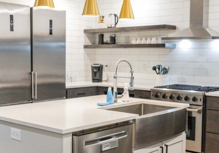 Modern kitchen with stainless steel appliances, white countertops, and wood shelving.