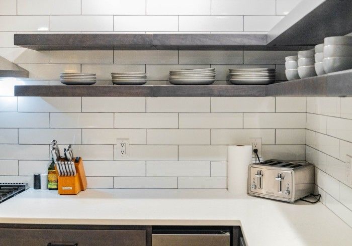 Kitchen with white subway tile backsplash, dark wood shelves, and countertop with dishes and toaster.
