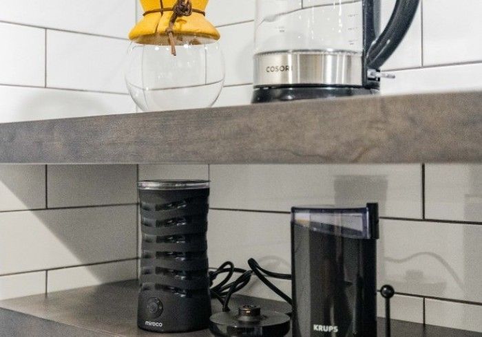 Coffee station with pour-over, electric kettle, frother, and grinder on a shelf.