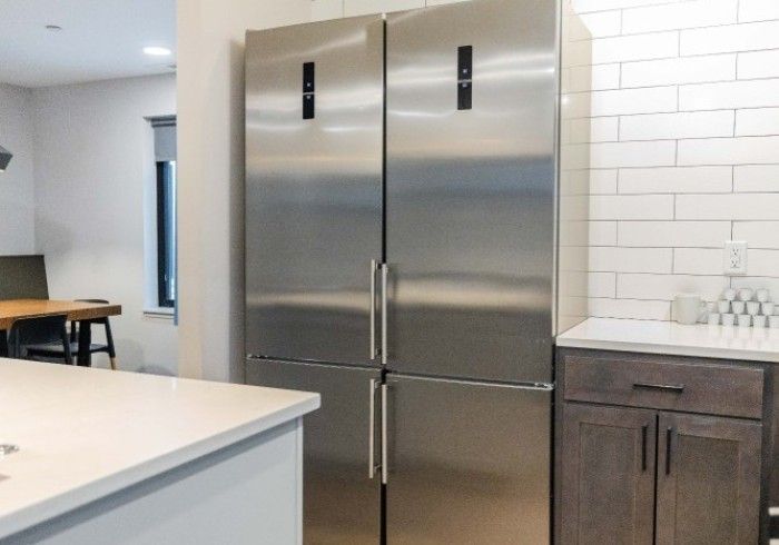 Stainless steel four-door refrigerator in a modern kitchen with white and dark wood cabinets.
