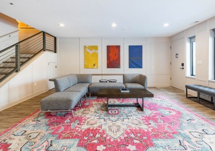 Living room with gray sectional sofa, colorful rug, modern art, and staircase.