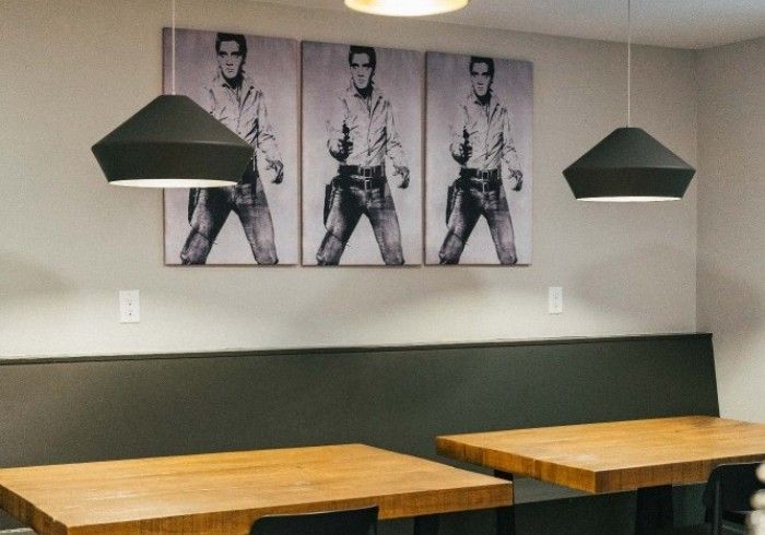 A dining area with wooden tables, black pendant lights, and an Elvis Presley triptych above a bench.