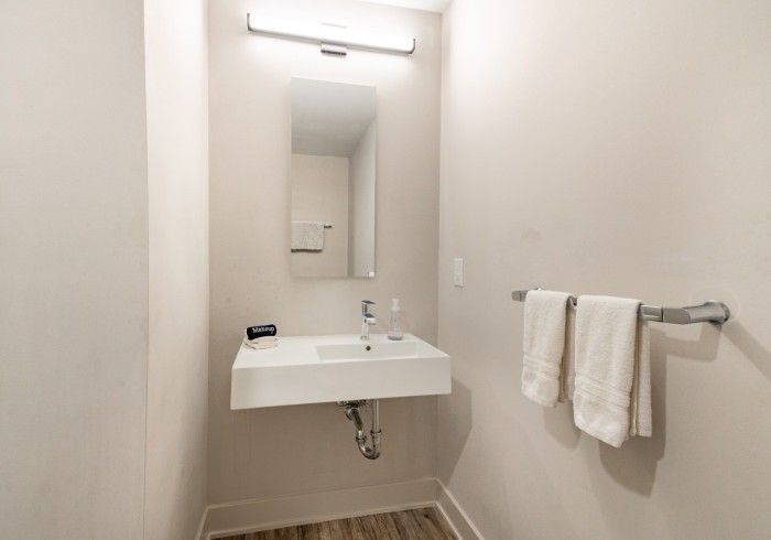 A small bathroom with a white sink, mirror, and two white towels. Beige walls.
