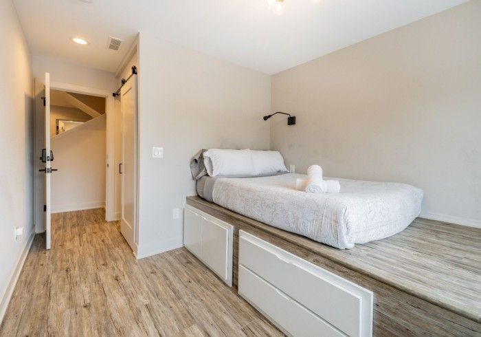 Bedroom with raised bed, drawers, and a pathway leading to a door and stairs.