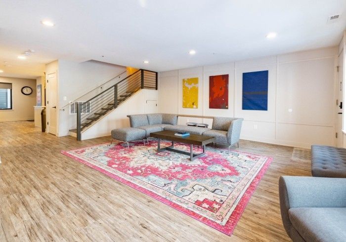 Modern living room with a gray sectional sofa, colorful art, and a pink patterned rug.