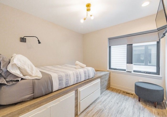 Bedroom with a bed on a raised platform, window with blinds, and a small stool.