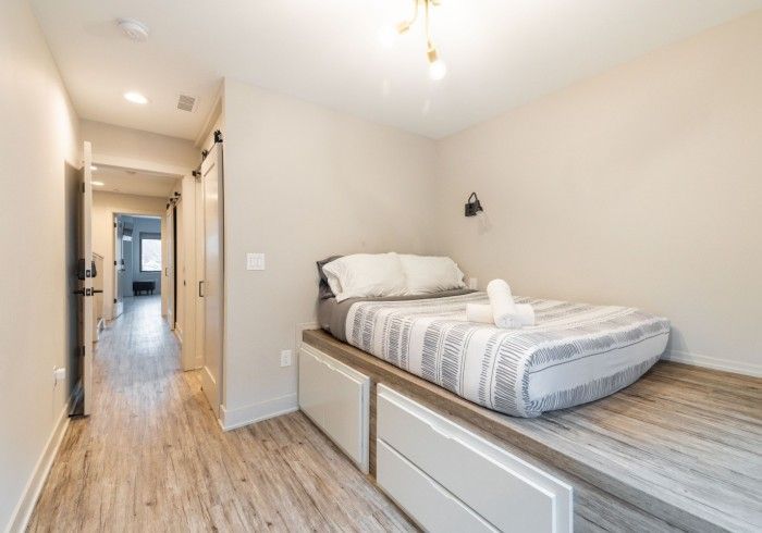 Bedroom with bed on platform with drawers; hallway visible.