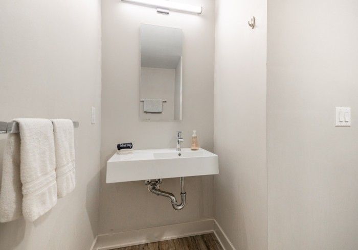 Small powder room with white walls, floating sink, mirror, towel bar, and light fixture.