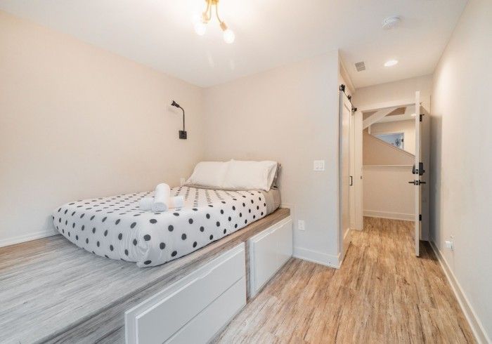 Bedroom with platform bed, drawers, and hallway with open door, light wood floors, neutral walls.