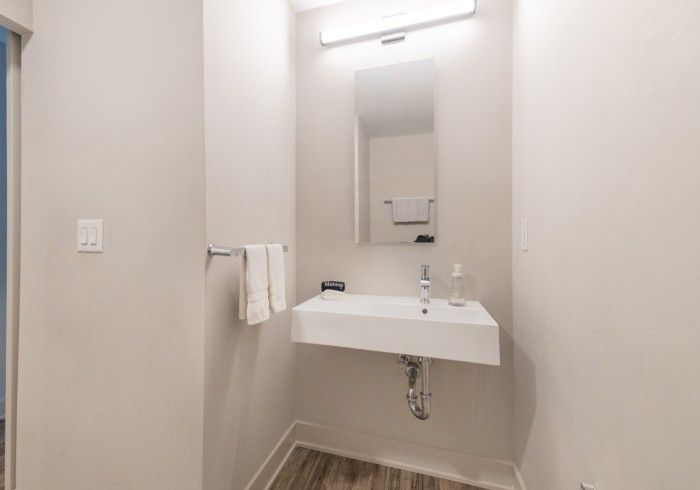 Small, modern bathroom with a white sink, mirror, and towel rack; beige walls and wood-look floor.