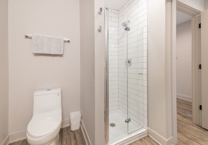 Bathroom with a white toilet, glass shower, towel rack, and open doorway to another room.
