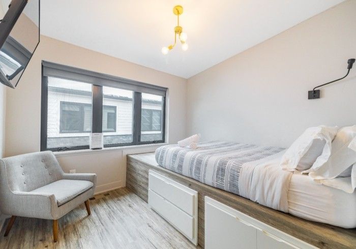 Bedroom with a bed on a platform, a chair, and a window with blinds.