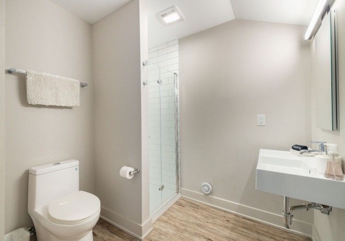 Small, neutral-toned bathroom with toilet, sink, and glass shower. Towel rack and mirror present.