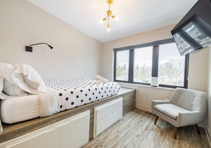 Bedroom with polka dot bed, window, chair, and mounted TV.