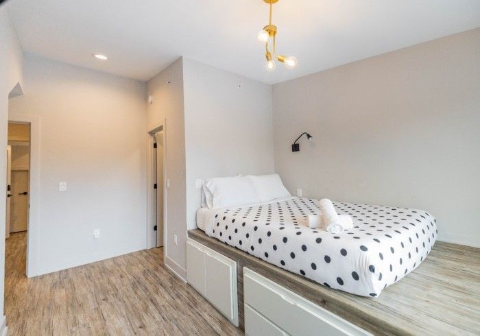 Bedroom with raised bed, polka-dot bedding, white and gray walls, wooden floor, and modern light fixtures.
