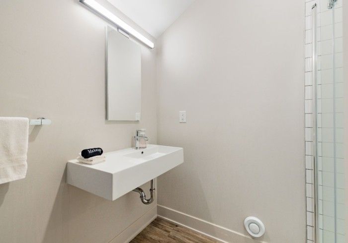 Modern bathroom with floating white sink, mirror, shower, towel rack, and wooden floor.