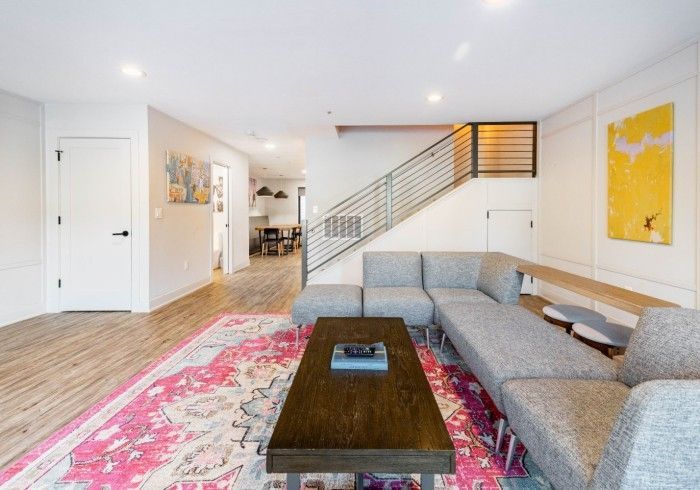 Modern living room with sectional sofa, rug, and artwork. Staircase, wooden floor.