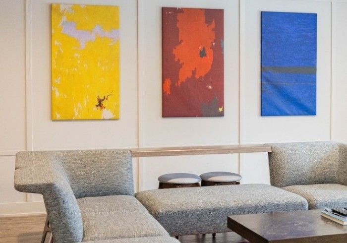 Living room with gray sofa, ottoman, and three abstract paintings: yellow, red, and blue.