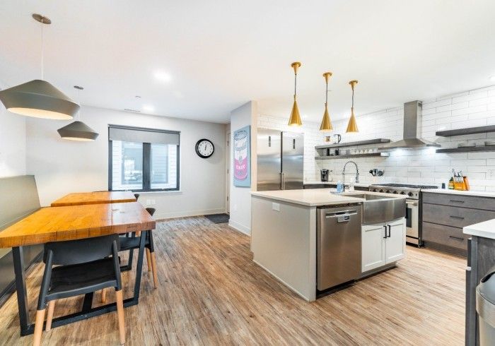 Modern kitchen with island, stainless steel appliances, dining table, wood floors, and pendant lights.