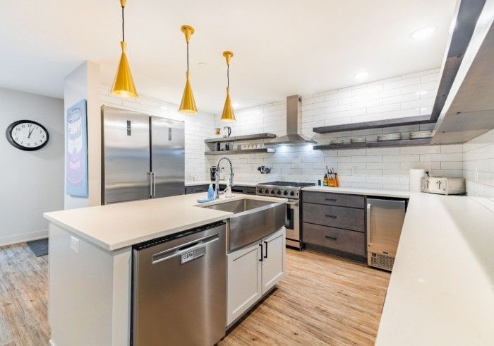 Modern kitchen with stainless steel appliances, white countertops, and wood flooring.