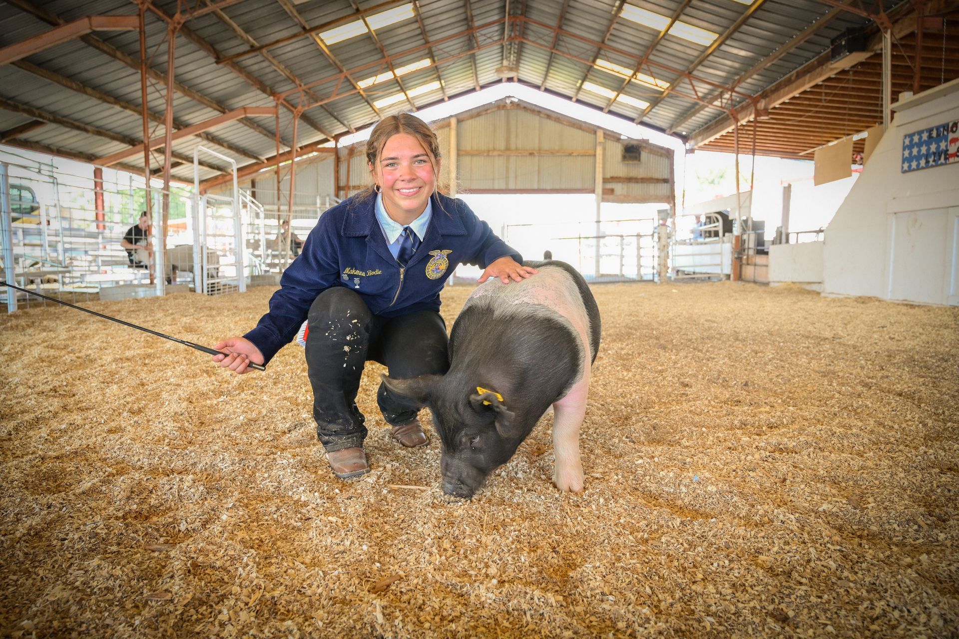 A woman is kneeling next to a pig in a barn.