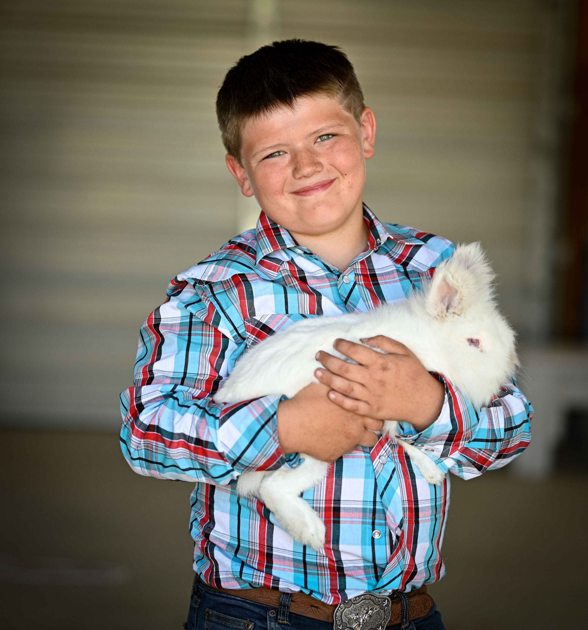 A young boy in a plaid shirt is holding a white rabbit